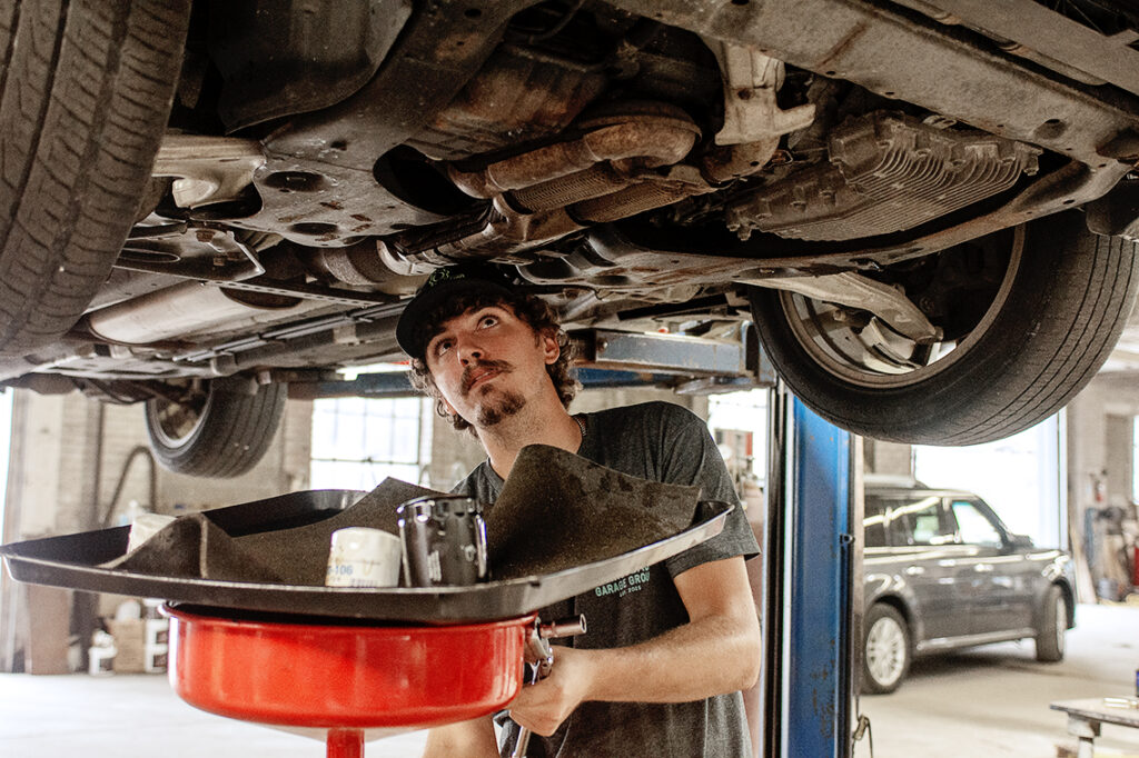 Technician draining oil from a lifted vehicle during an oil change in Covington, IN