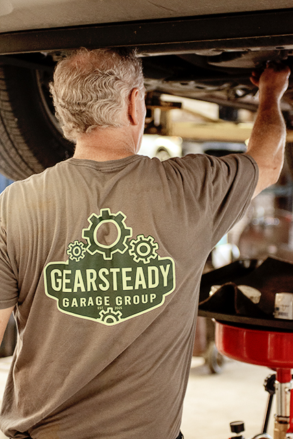 Technician reaching up to transmission components under a lifted vehicle