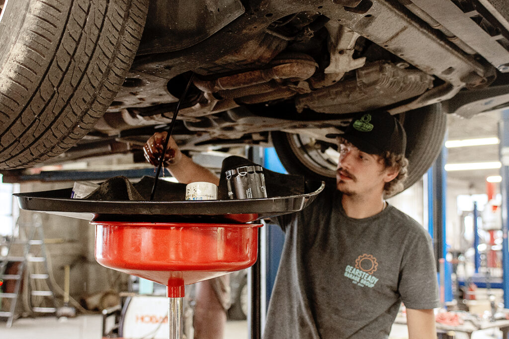 Young technician draining fluid underneath a raised car